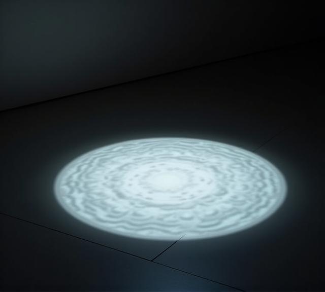 美術館の暗い展示室の床に置かれた、水面のように揺らめく円形の光の作品